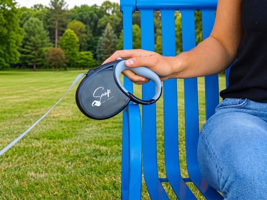 Hand holding the retractable dog leash handle just above a park bench arm, ready to clip on