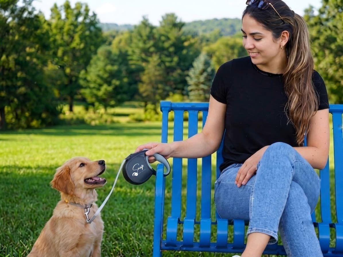 Woman relaxing hands-free and smiling at her puppy on the leash clipped to a park bench
